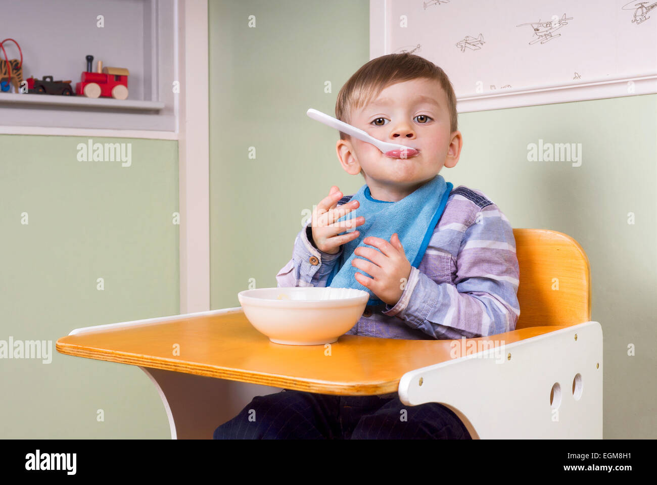 two year old boy sitting in his chair eating yoghurt and making fun Stock Photo