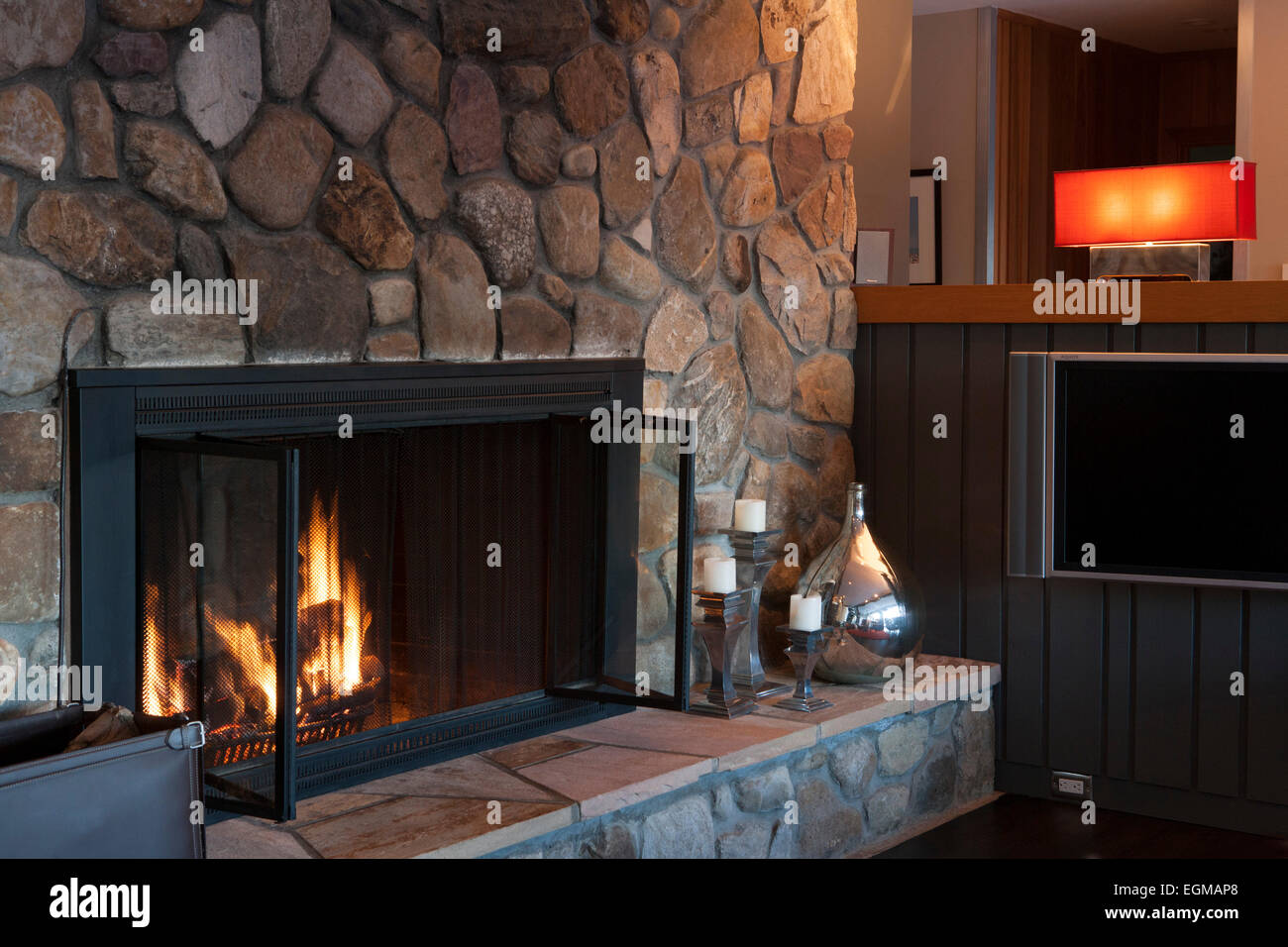 Fire In Stone Fireplace With Red Lamp In Background Stock Photo