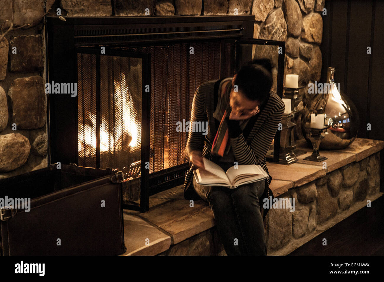 Woman Reading Next to Fireplace Stock Photo