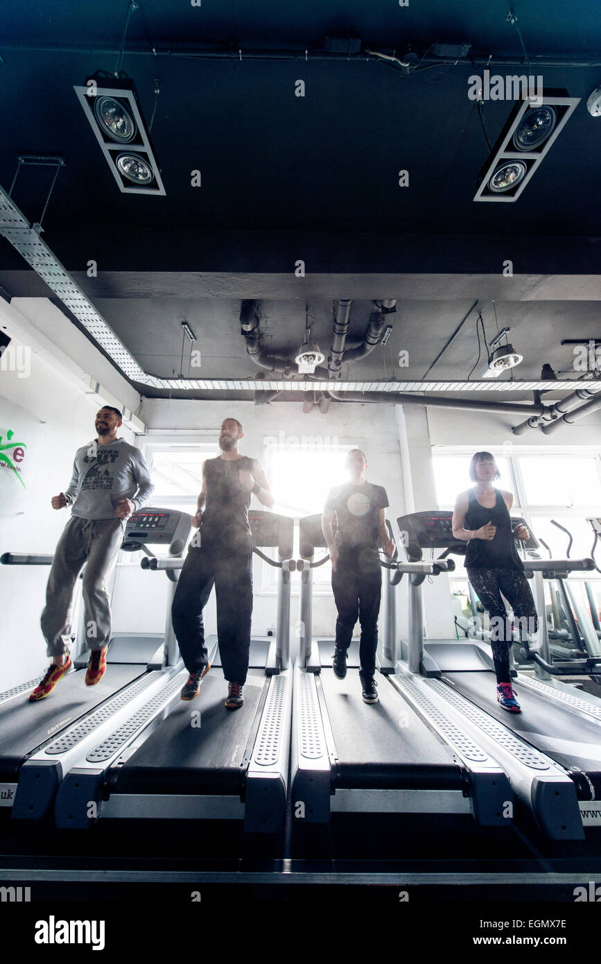 wide angle shot of four fitness professionals / trainers, jogging on running machines / treadmills inside a gym during the day Stock Photo
