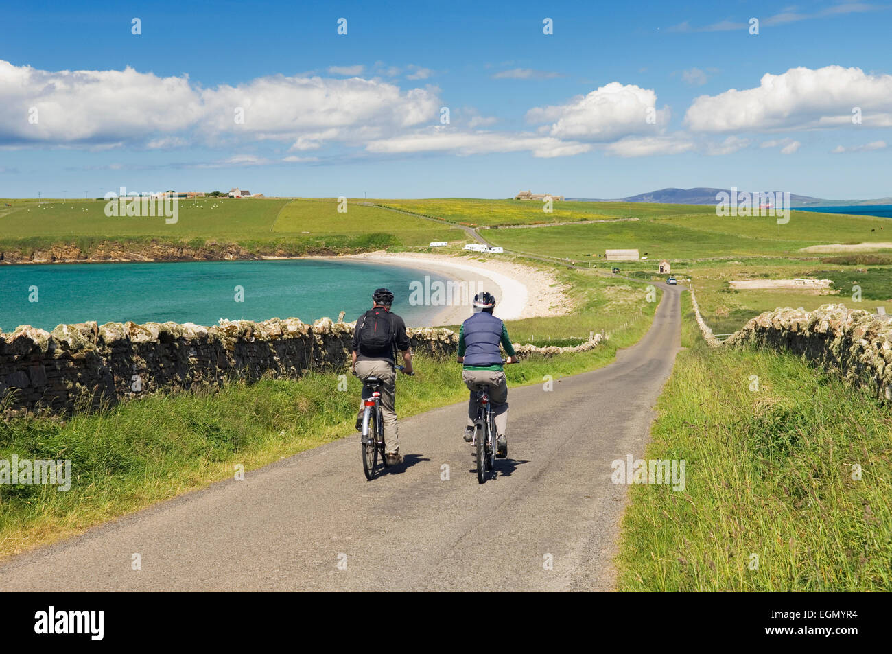 Young man and woman cycling along a quiet road on South Ronaldsay, Orkney Islands, Scotland. Stock Photo