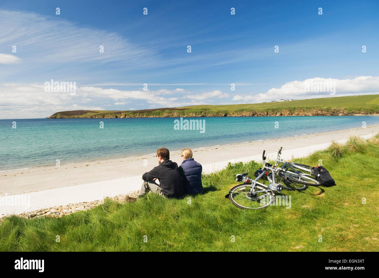 Young man and woman resting beside their bicycles while cycling on South Ronaldsay, Orkney Islands, Scotland. Stock Photo