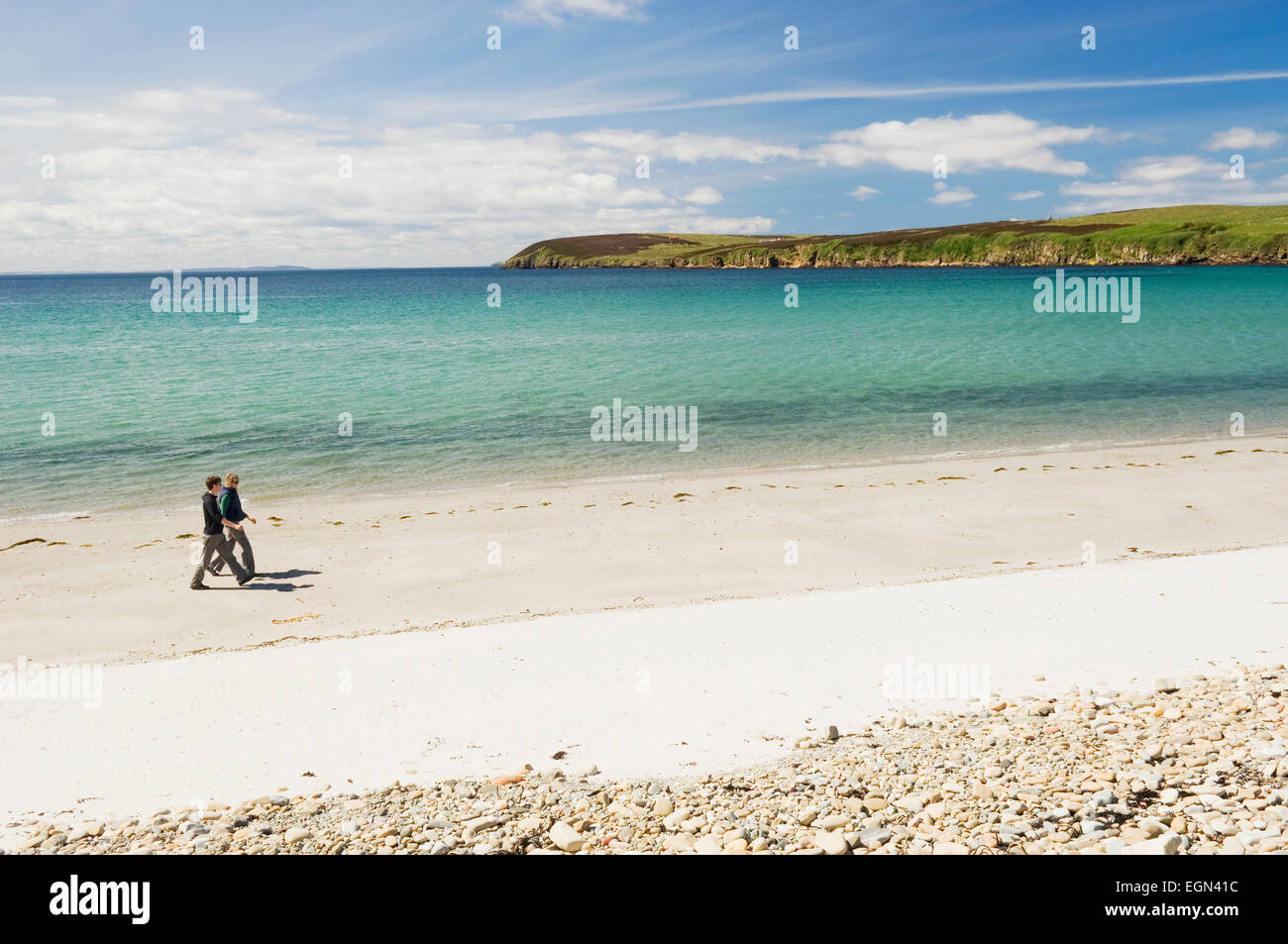 Young woman and man walking on a sandy beach in summer sunshine, Sands of Wright, South Ronaldsay, Orkney Islands, Scotland. Stock Photo
