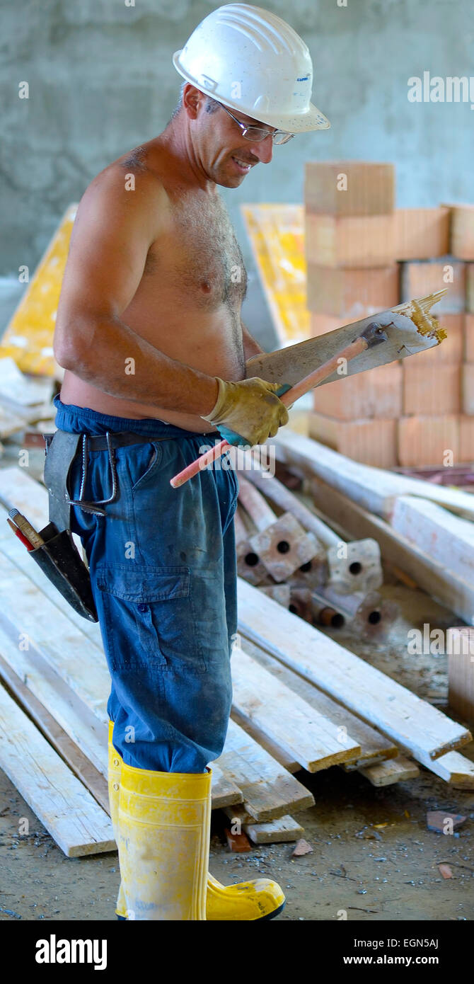 Construction worker removing nail from wooden plank using hammer. Focus is on the tools and tiles. Stock Photo