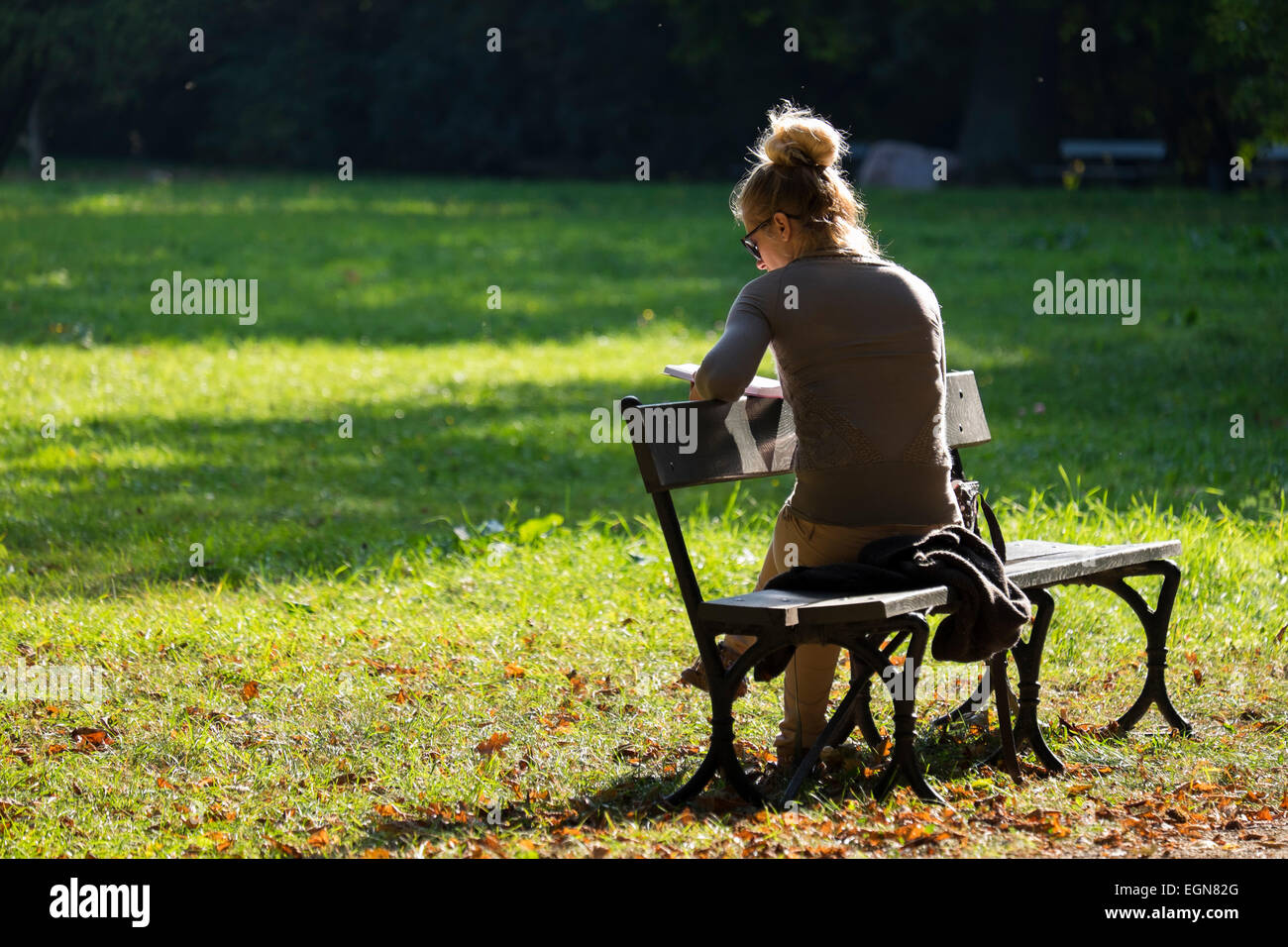 Attractive young lady reading a book on a warm sunny afternoon in Lazienkowski Park, Warsaw Stock Photo