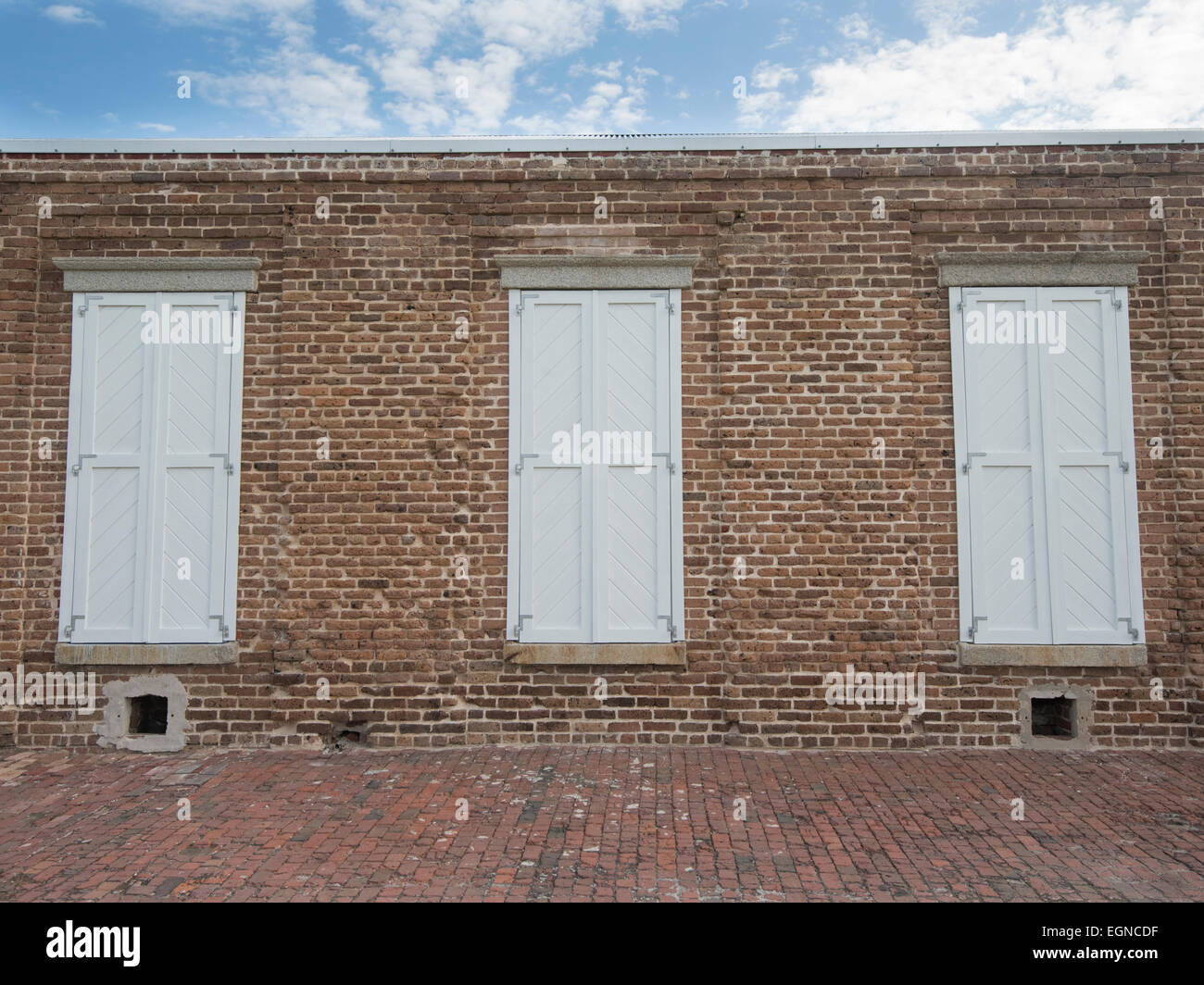 Three white shutters on a red brick building under a blue sky Stock Photo