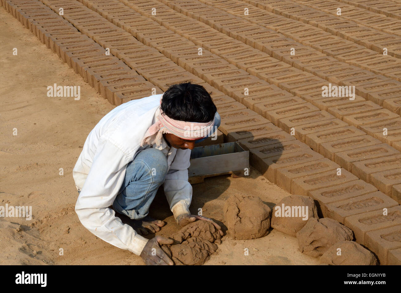 Indian man squatting on the ground making hand made bricks from clay mud Madhya Pradesh India Stock Photo