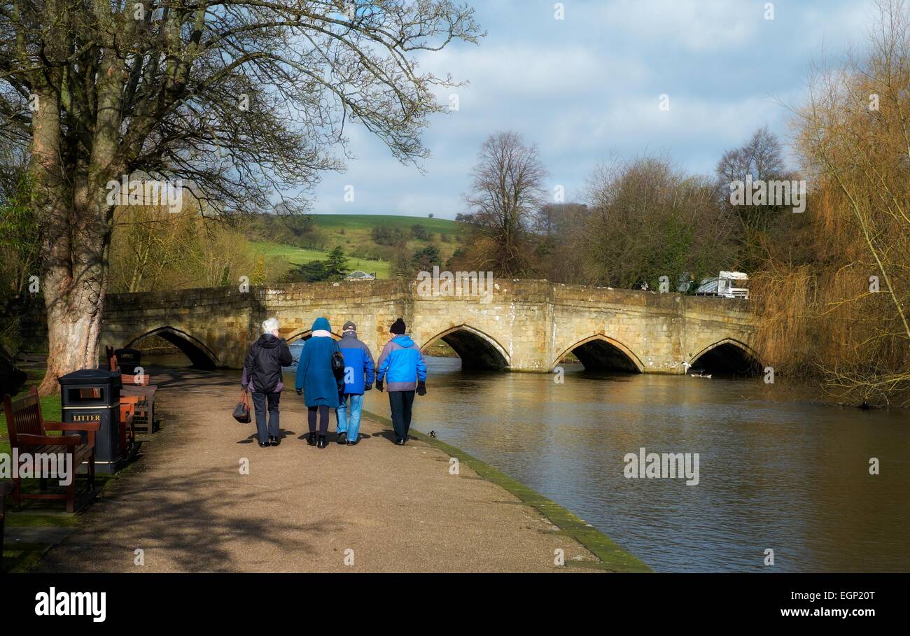 Elderly senior people walking along the river wye in bakewell with the 13th century bridge in the background Derbyshire England Stock Photo