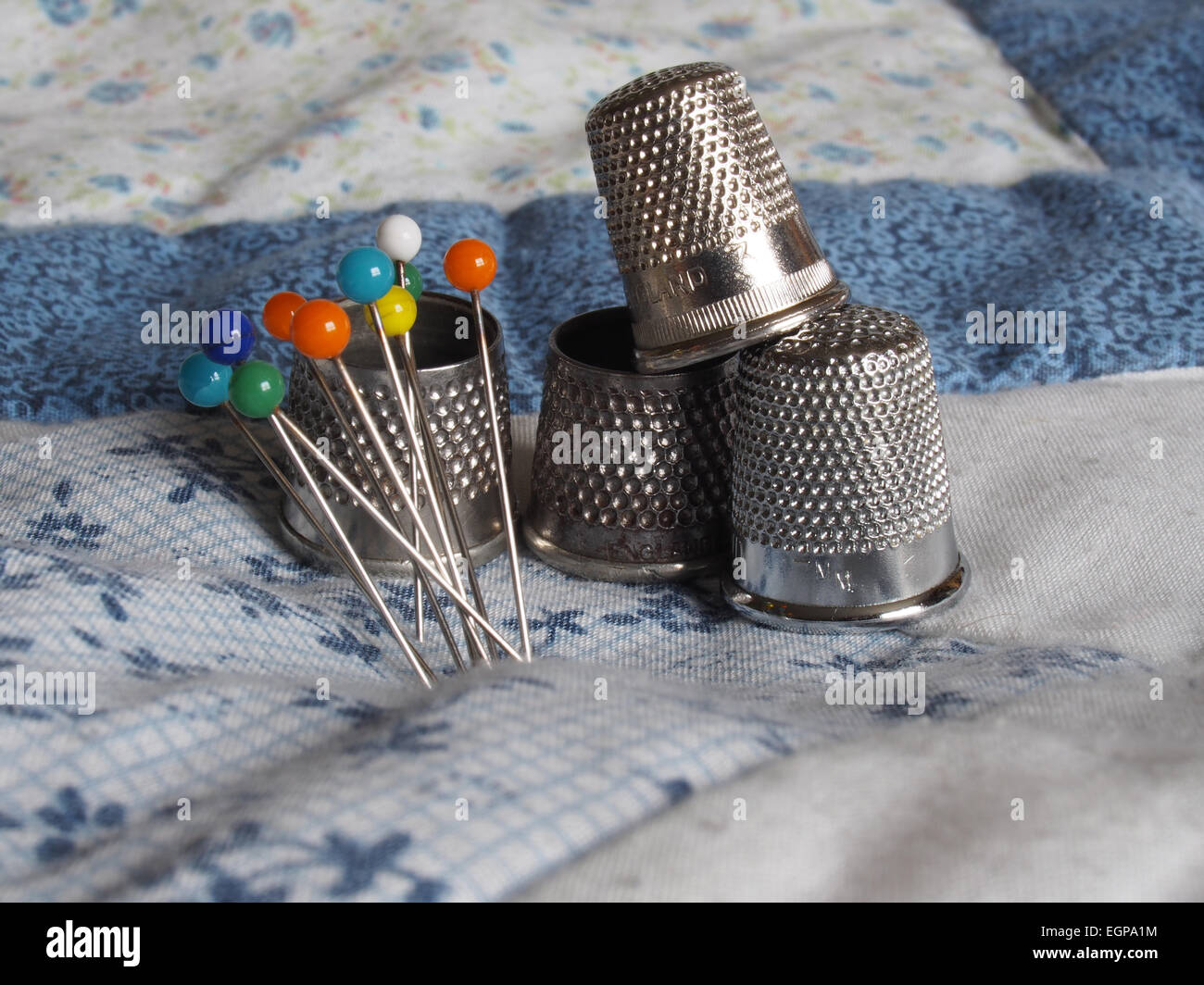 Four different thimbles and a group of coloured pins on some patchwork Stock Photo