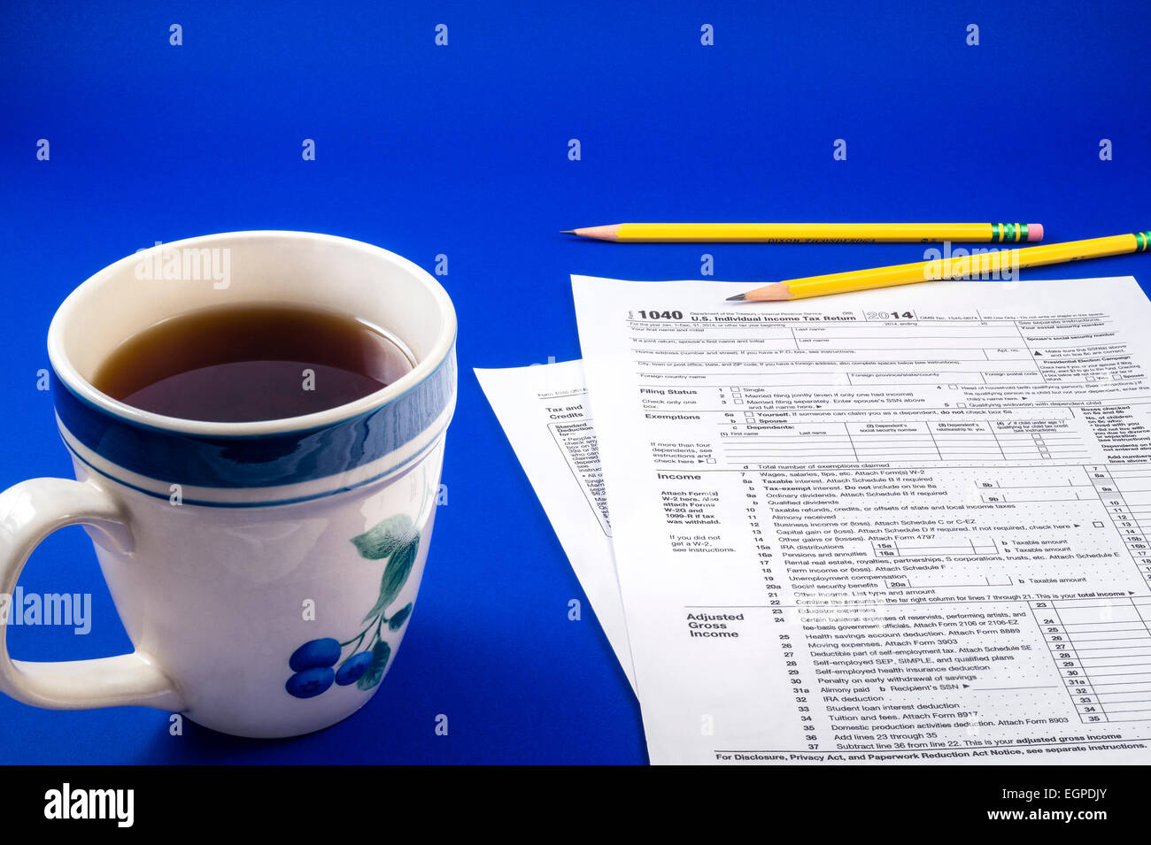 Relaxing cup of black coffee in a stoneware mug with pencils and IRS 1040 tax form on blue background Stock Photo