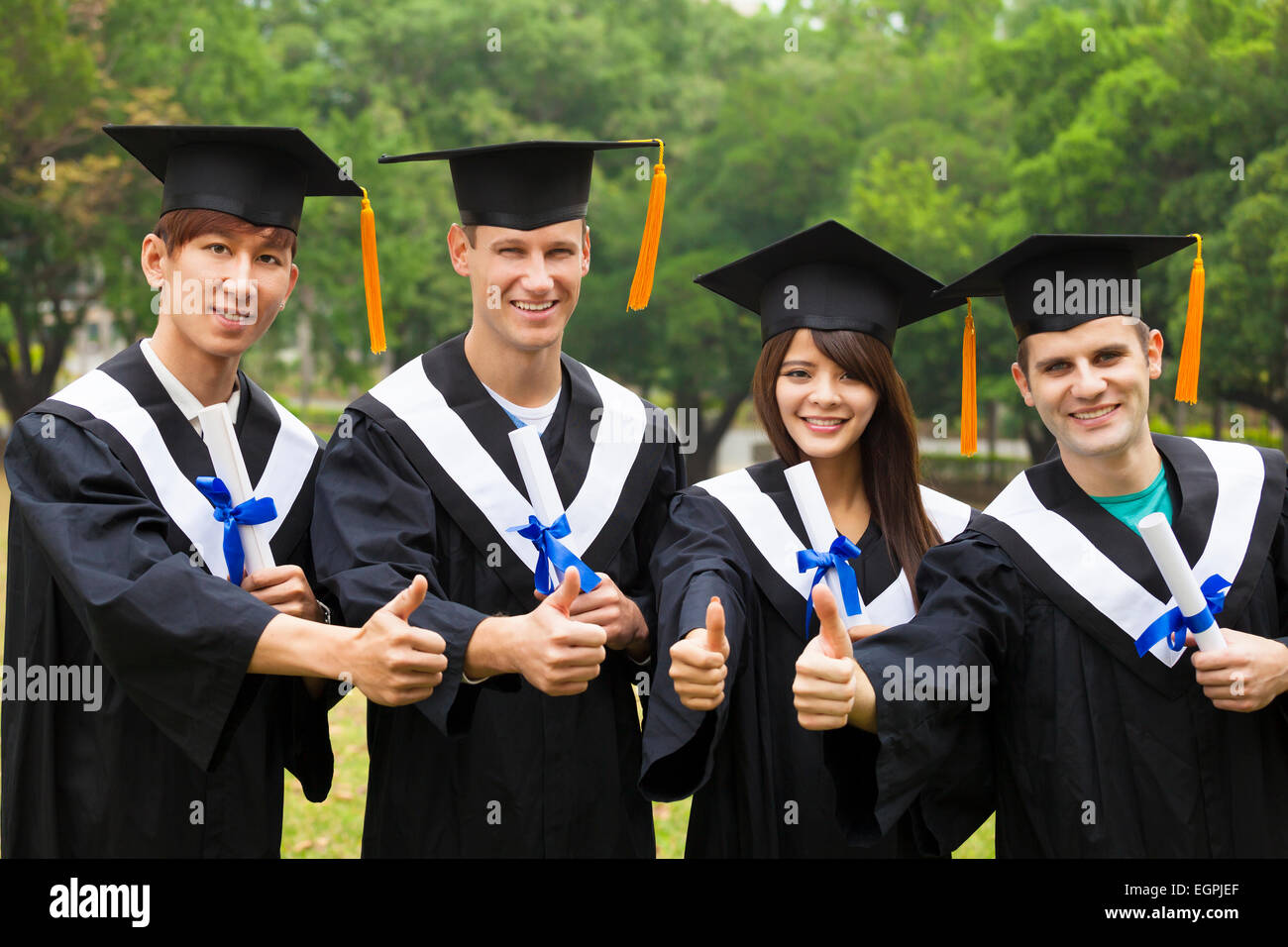 happy students in graduation gowns showing diplomas with thumbs up Stock Photo