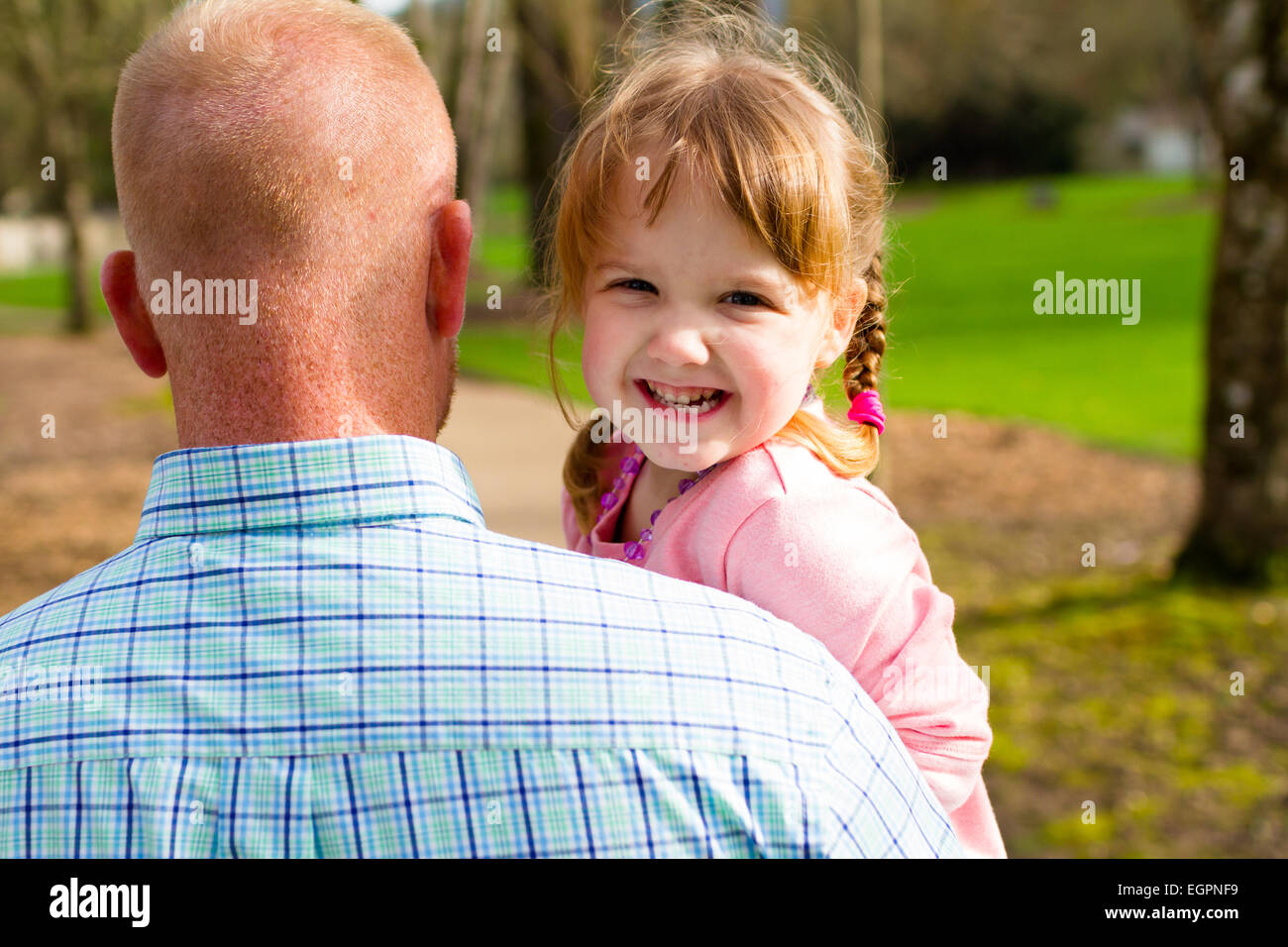 Daughter being held by her parent while walking at a park. Stock Photo