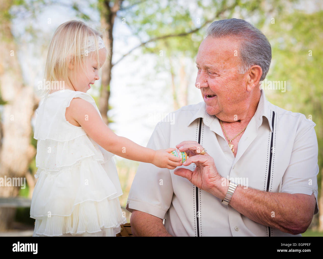 Cute Baby Girl Handing Easter Egg to Grandfather Outside at the Park. Stock Photo