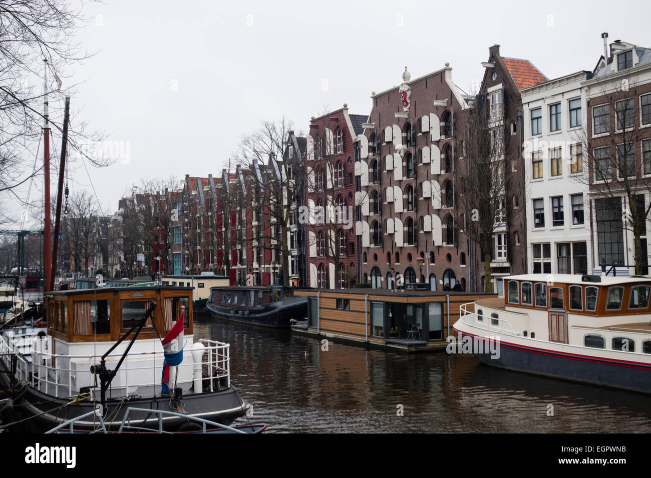 Historic boats lining a typical Amsterdam canal, with restored warehouses converted to