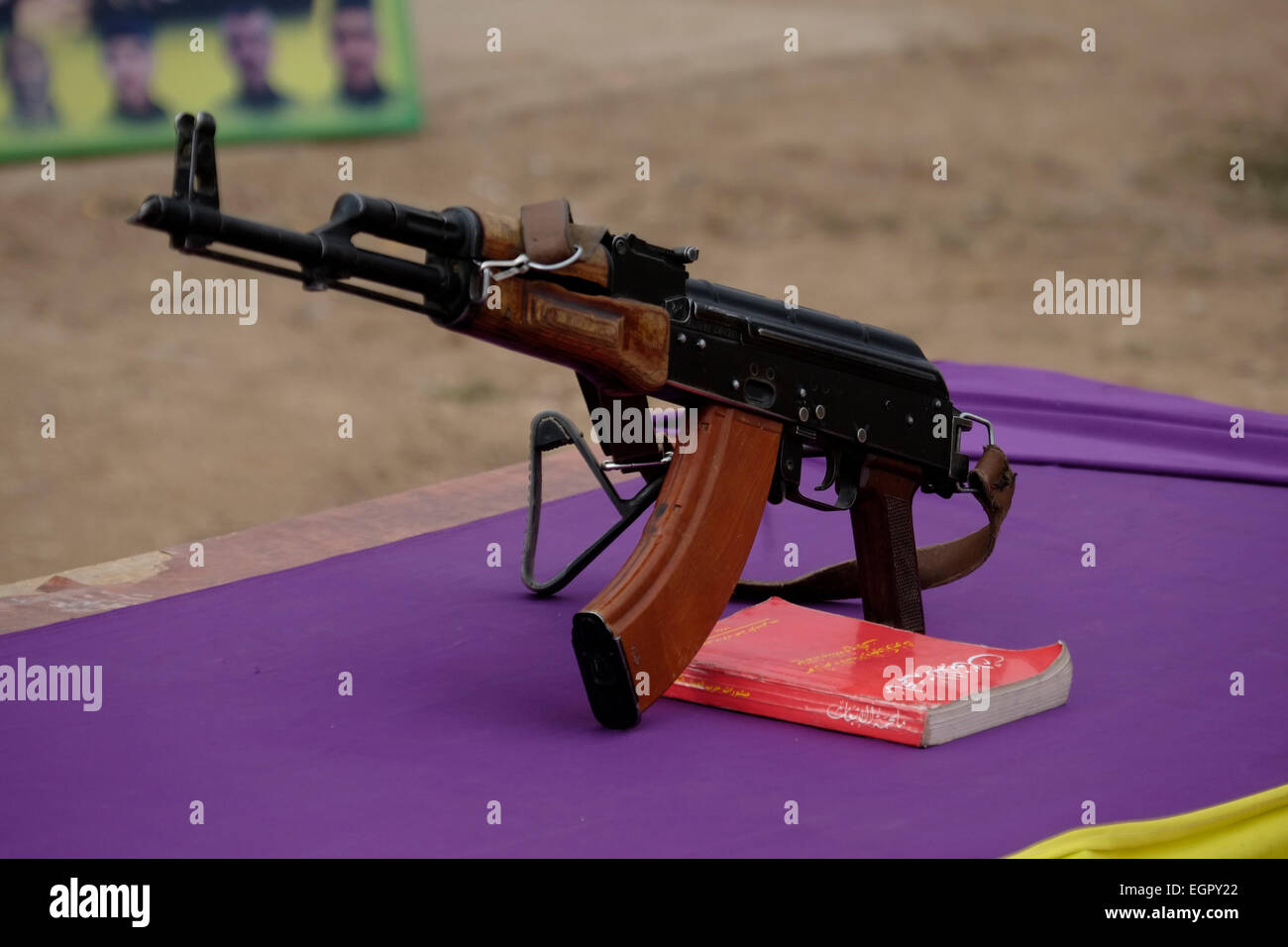 A Kalashnikov ak-47 rifle placed on a table with the Political Thought of Abdullah Ocalan Kurdish leader and one of the founding members of the militant Kurdistan Workers' Party PKK during swearing ceremony of Kurdish fighters YPG in a recruitment camp in Al Hasakah or Hassakeh district in northern Syria Stock Photo