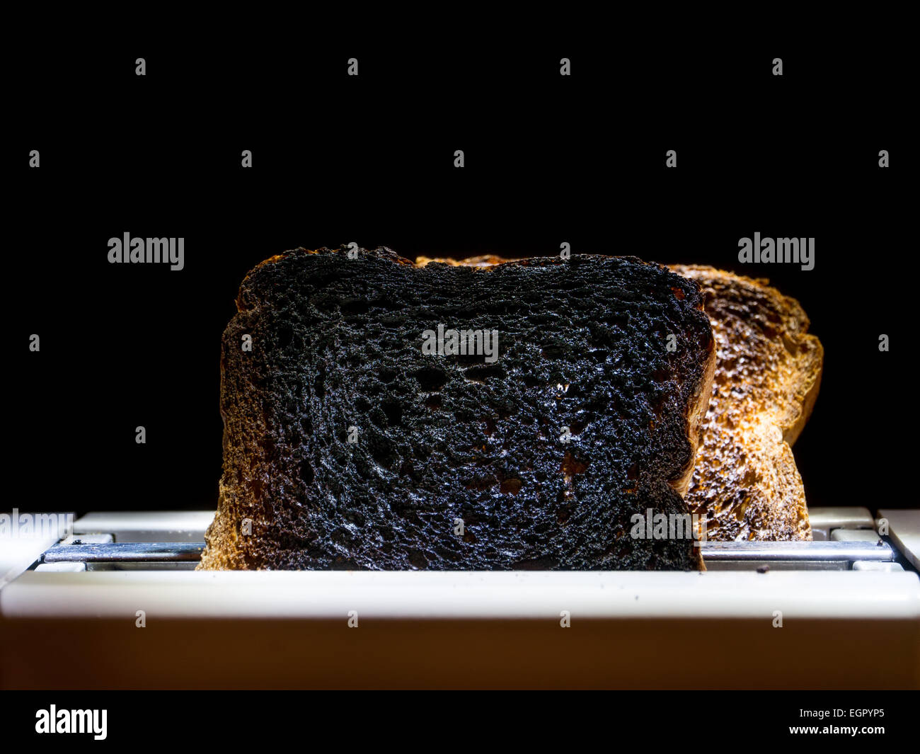 Two burnt toast slices sticking out of toaster over black background Stock Photo