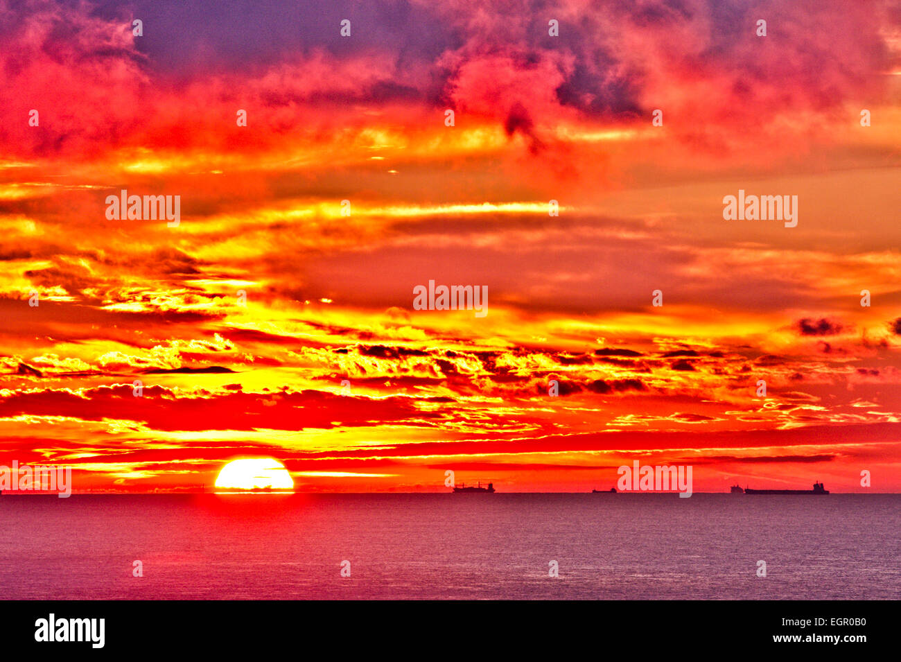 The English Channel seen from dover with the sunrise in a spectacular red and yellow sky over Calais and the French coast. Tankers sailing on horizon. Stock Photo