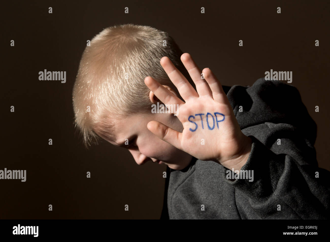 Upset abused frightened little child (boy), stop hand jesture close up horizontal dark portrait with copy space Stock Photo