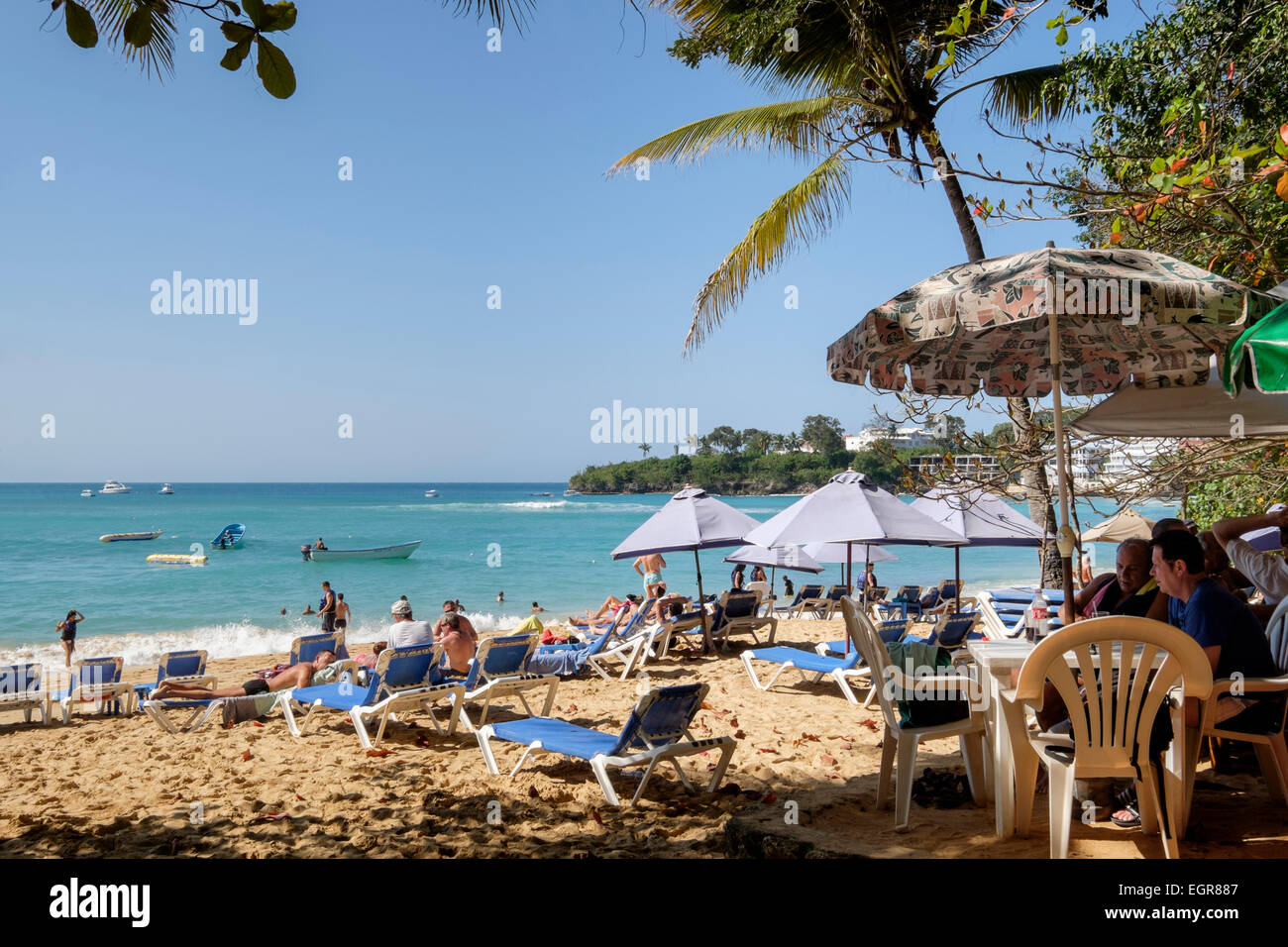 Beach bar and tourists on sandy beach with sea beyond in holiday resort of Sosua, Puerto Plata, Dominican Republic, Caribbean Stock Photo
