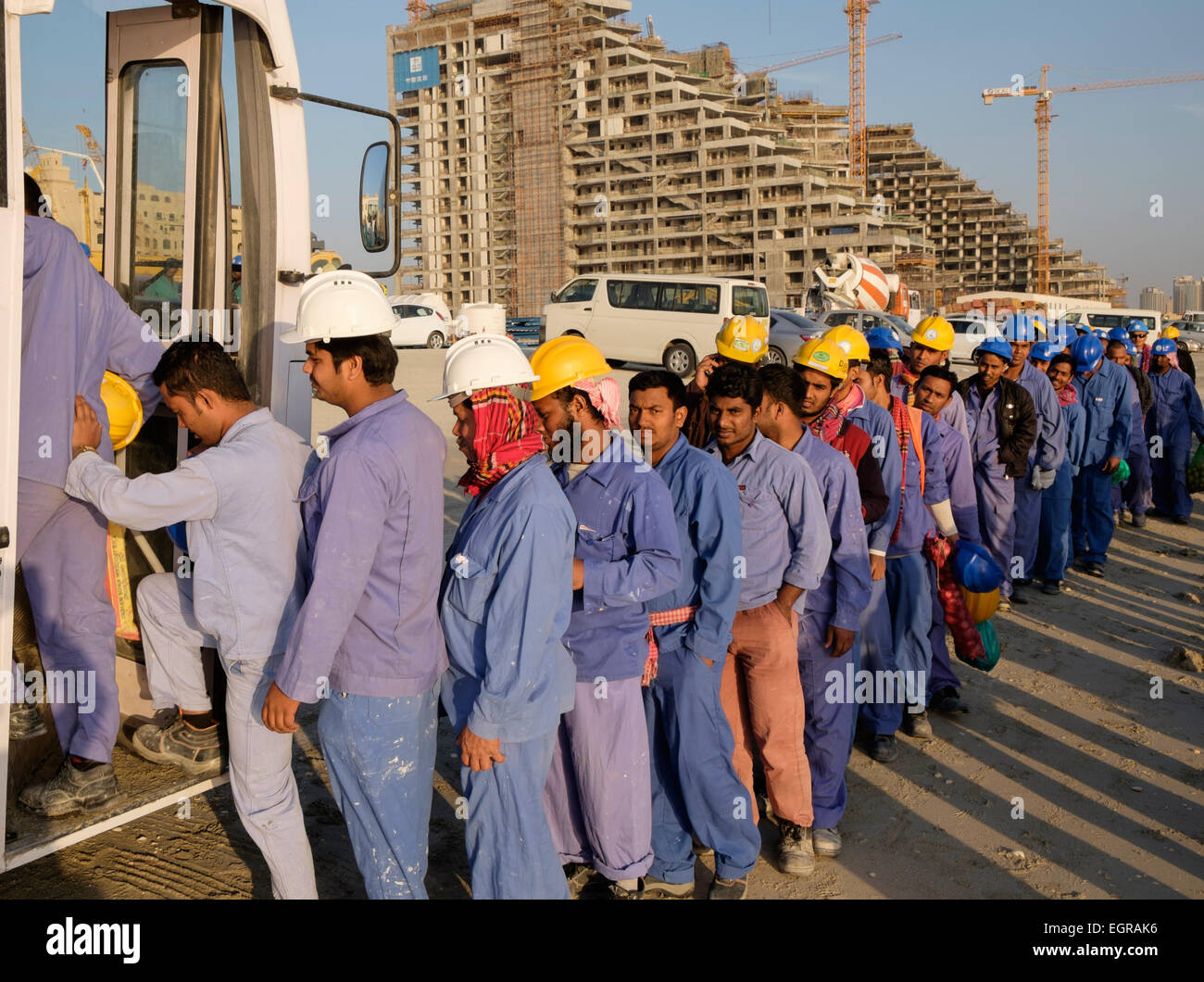 Construction workers queuing to get on bus to living quarters at end of