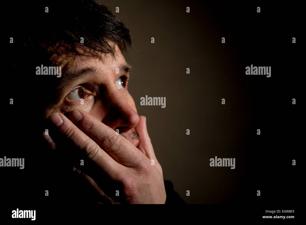 Close up of man with his head in his hand, his eyes are looking away in fear/shock. Stock Photo