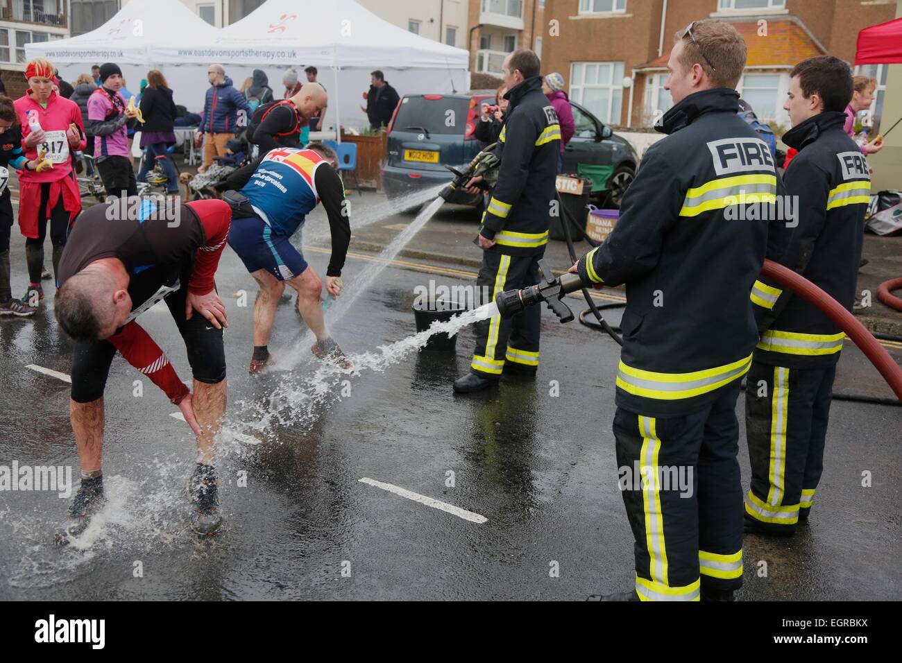 Seaton, Devon, UK. 1 March,  2015:  Firefighters hose mud of the runners after they have finished the Annual 'Grizzly' race.  This gruelling 20 mile cross country race traces its way along cliff paths, across hilly terrain, ascends and descends more than 3,500 ft and presents runners with muddy bogs, waist deep water and steep cliffs. The race, which is organised by the Axe Valley Runners, has attracted entrants from as far afield as Cyprus and the USA.  Credit:  Tom Corban/Alamy Live News Stock Photo