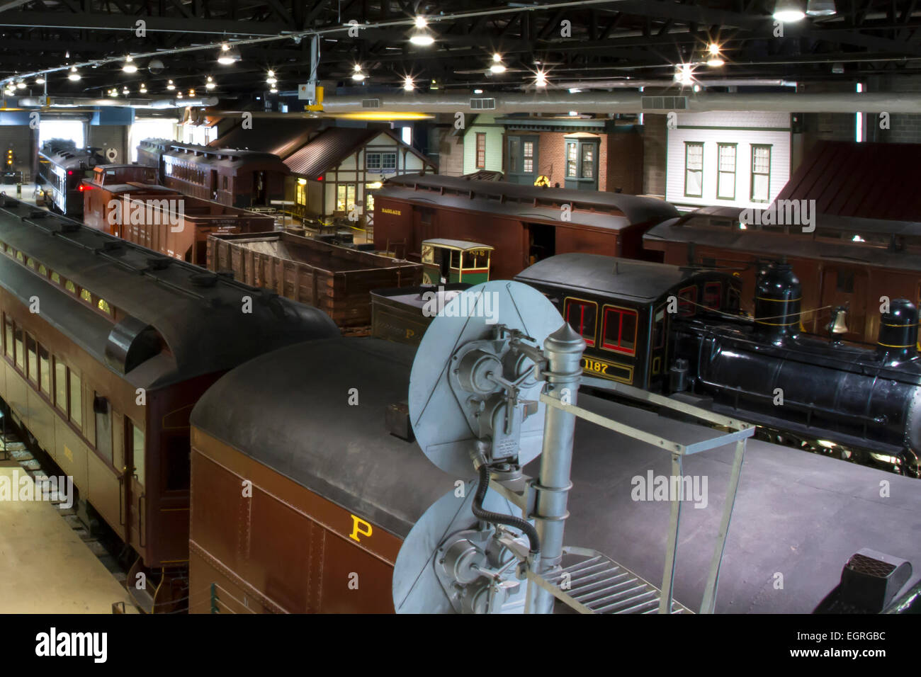 Antique train cars and support equipment on tracks near a platform of a model train station