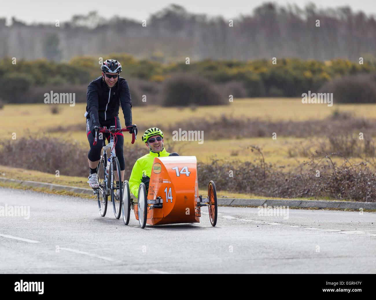 Two cyclists, one uses a conventional bicycle, the other, in a high vis jacket, is testing a recumbent prototype cycle. Stock Photo