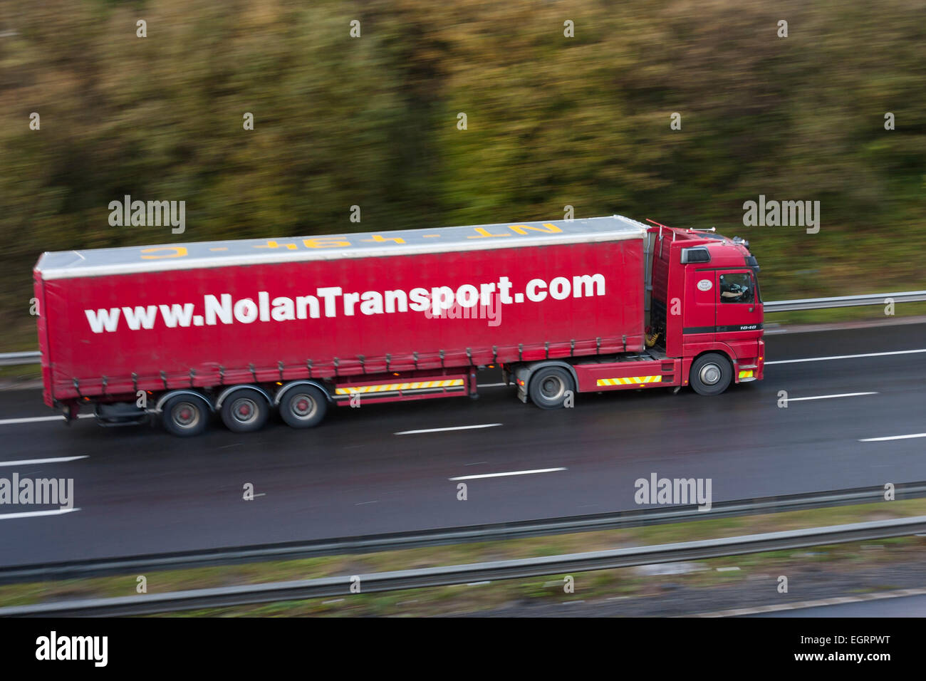 red articulated curtain-side sign written truck traveling at speed on wet motorway with blurred motion Stock Photo