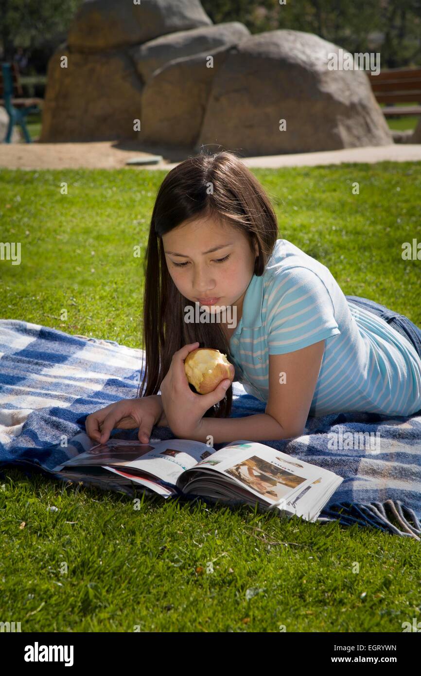 12 -13 year old mixed race Vietnamese/Caucasian girl reading magazine on grass park young person people Tween tweens  MR  © Myrleen Pearson Stock Photo