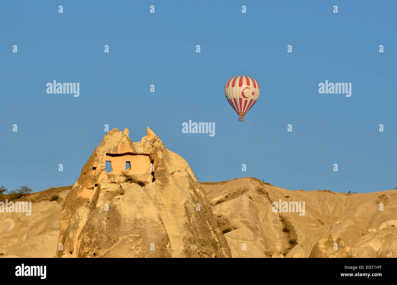 Hot air balloon flying over tufa rock formations and ancient cave dwellings, Goreme, Cappadocia, Turkey Stock Photo