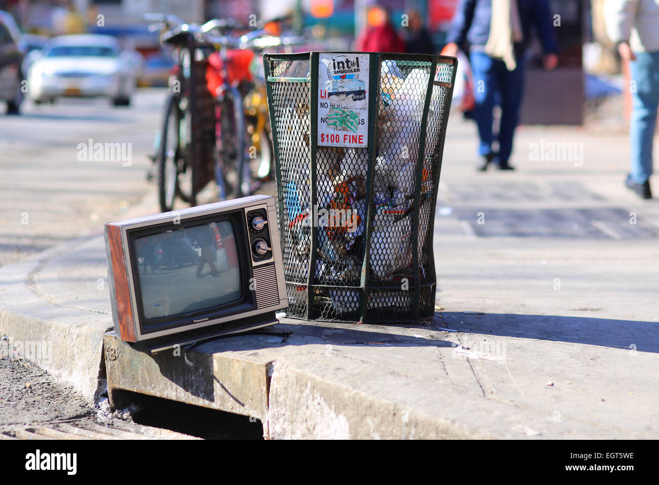 An abandoned analog tv lies next to a nyc garbage can Stock Photo