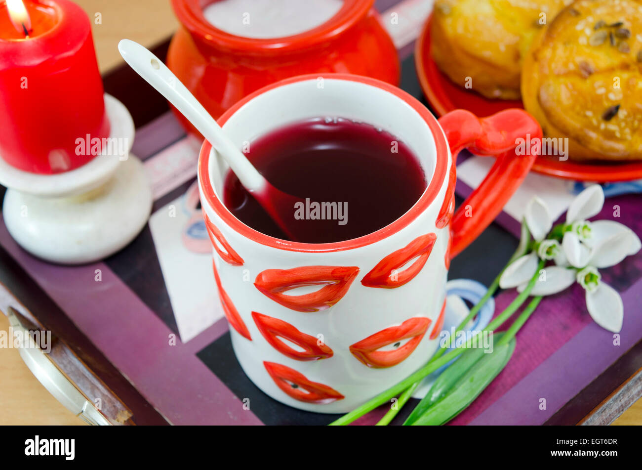 Lip patterned cup of tea on a tray with snowdrops, cornbread, sugar and a burning candle in the background Stock Photo