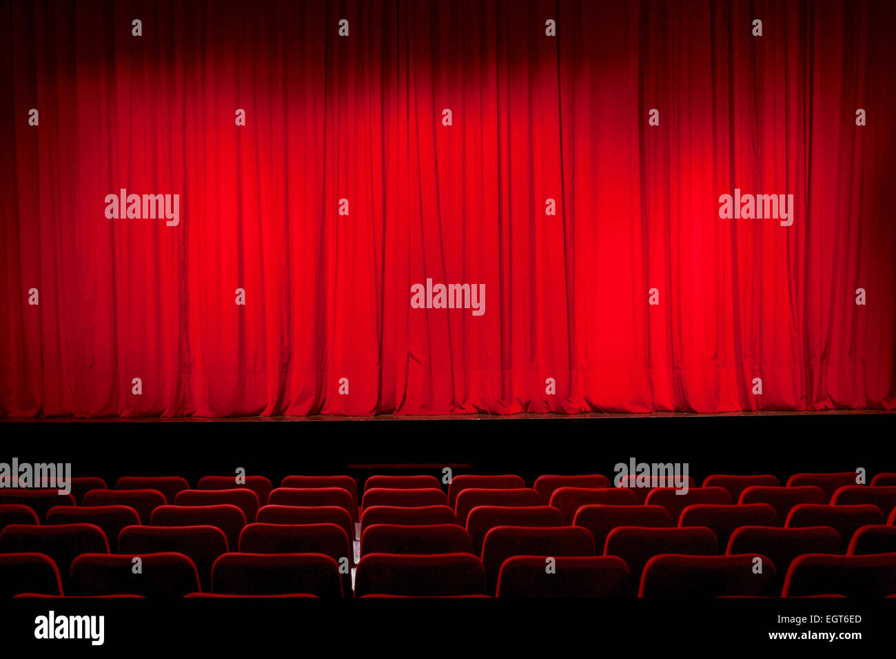 A theatre stage closed by a red curtain in a completely empty theatre ...