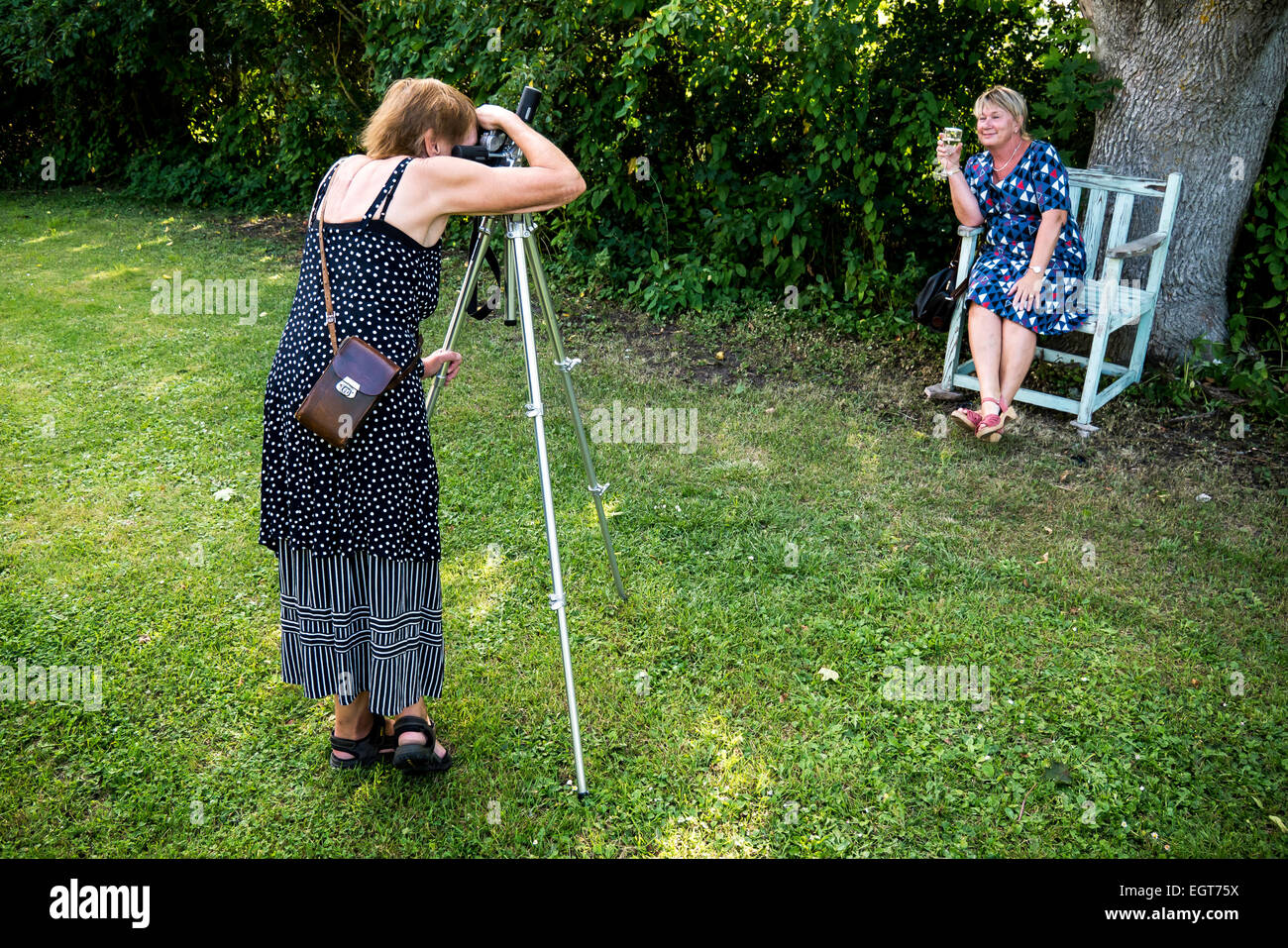 one woman takes a photo of woman sitting in a chair with a glass of wine Stock Photo