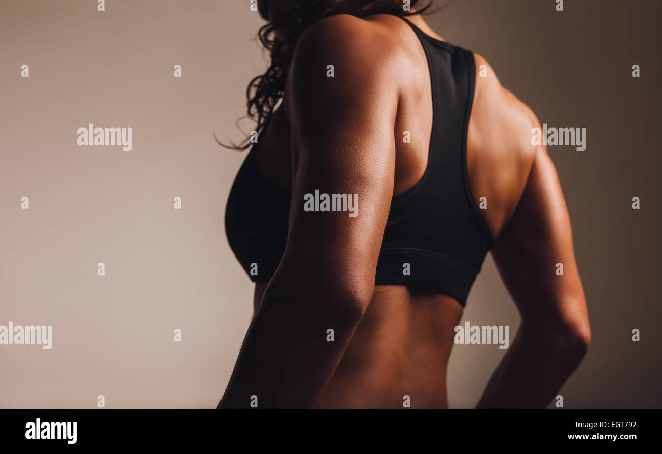 Back of a fit and muscular woman athlete in sports bra. Rear view of fitness female with muscular body. Highlighted on back. Stock Photo