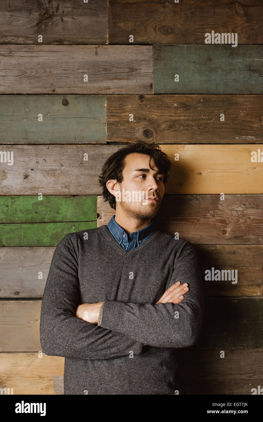 Handsome young business man leaning against a wooden wall with his arms crossed looking away. Stock Photo