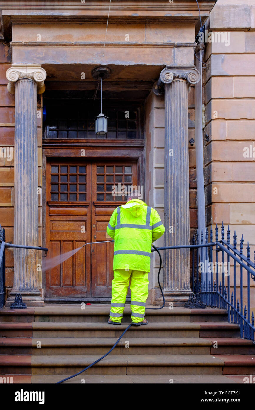 Workman using a high pressure washer to clan the bloom coloured sandstone facade of a building, Bath Street, Glasgow, Scotland Stock Photo