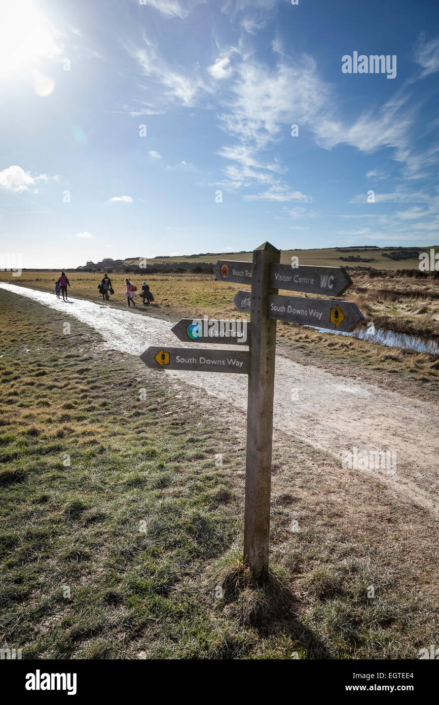 Day trippers make their way towards the beach at Cuckmere Haven ona sunny winter's day following the directions from the wooden Stock Photo