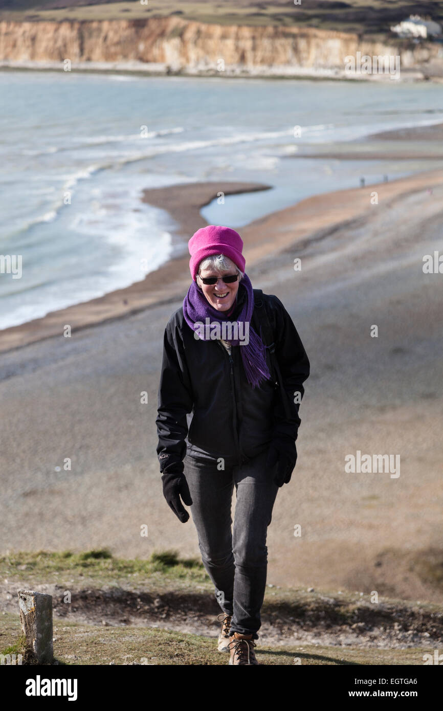 Woman climbs up the first of the Seven Sisters hills with the shingle beach and estuary of Cuckmere Haven below. Stock Photo