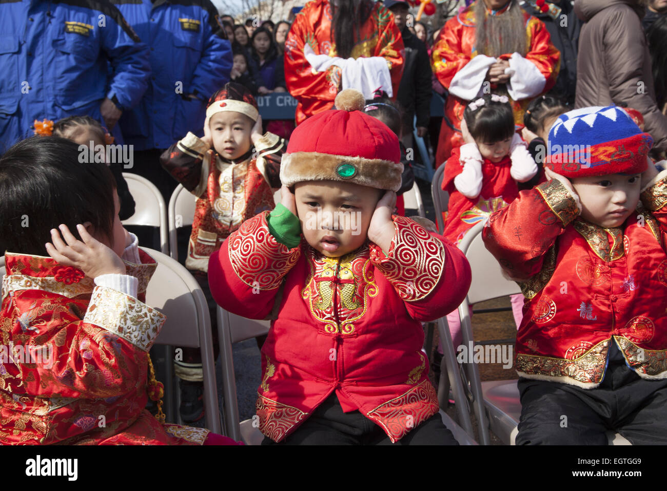 Chinese children in costumes at Chinese New Year celebration hold their ears during the very loud firecracker ceremony in the Chinatown neighborhood of Brooklyn, NY. Stock Photo