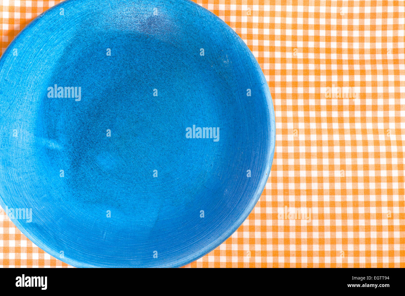 closeup to blue plate on orange checkered tablecloth Stock Photo
