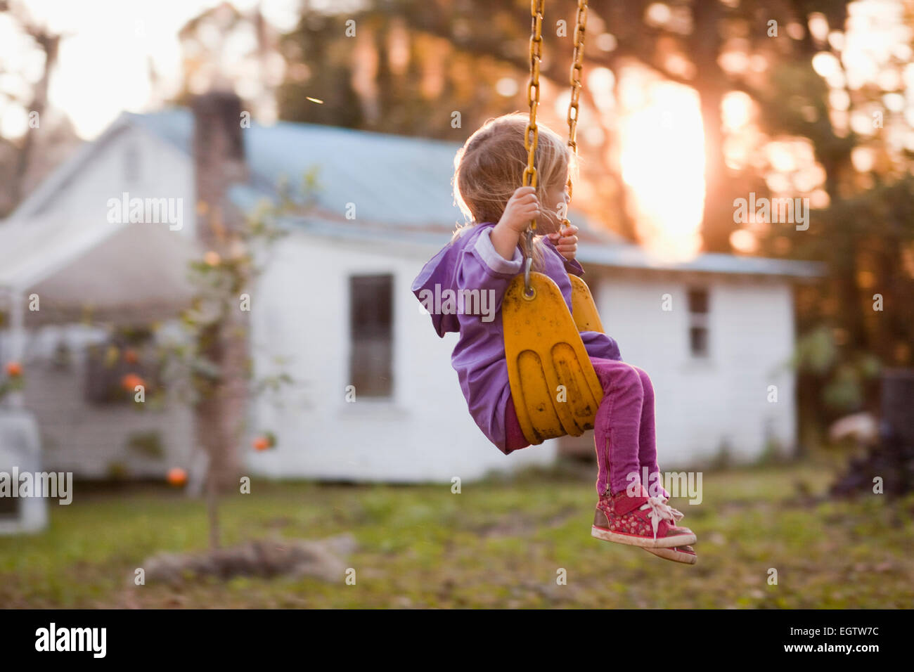 A young girl sits on a backyard swing. Stock Photo