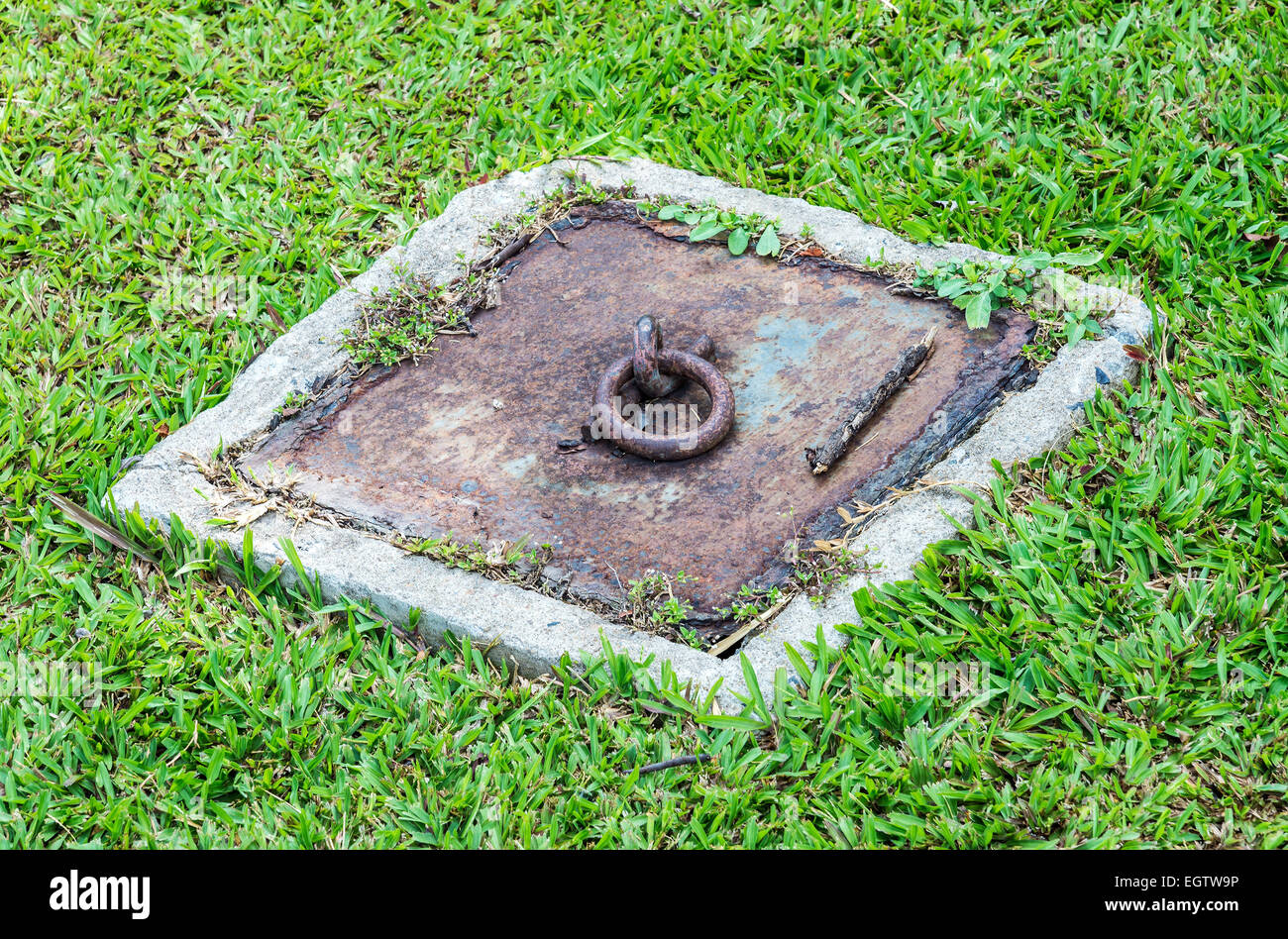 Rusty drain cap on the lawn in the urban park. Stock Photo