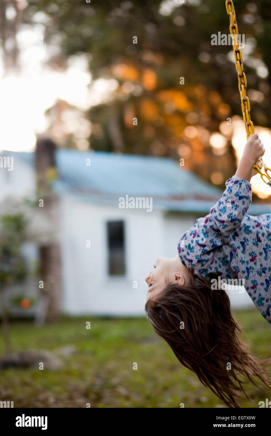A girl holding onto a swing in a backyard. Stock Photo