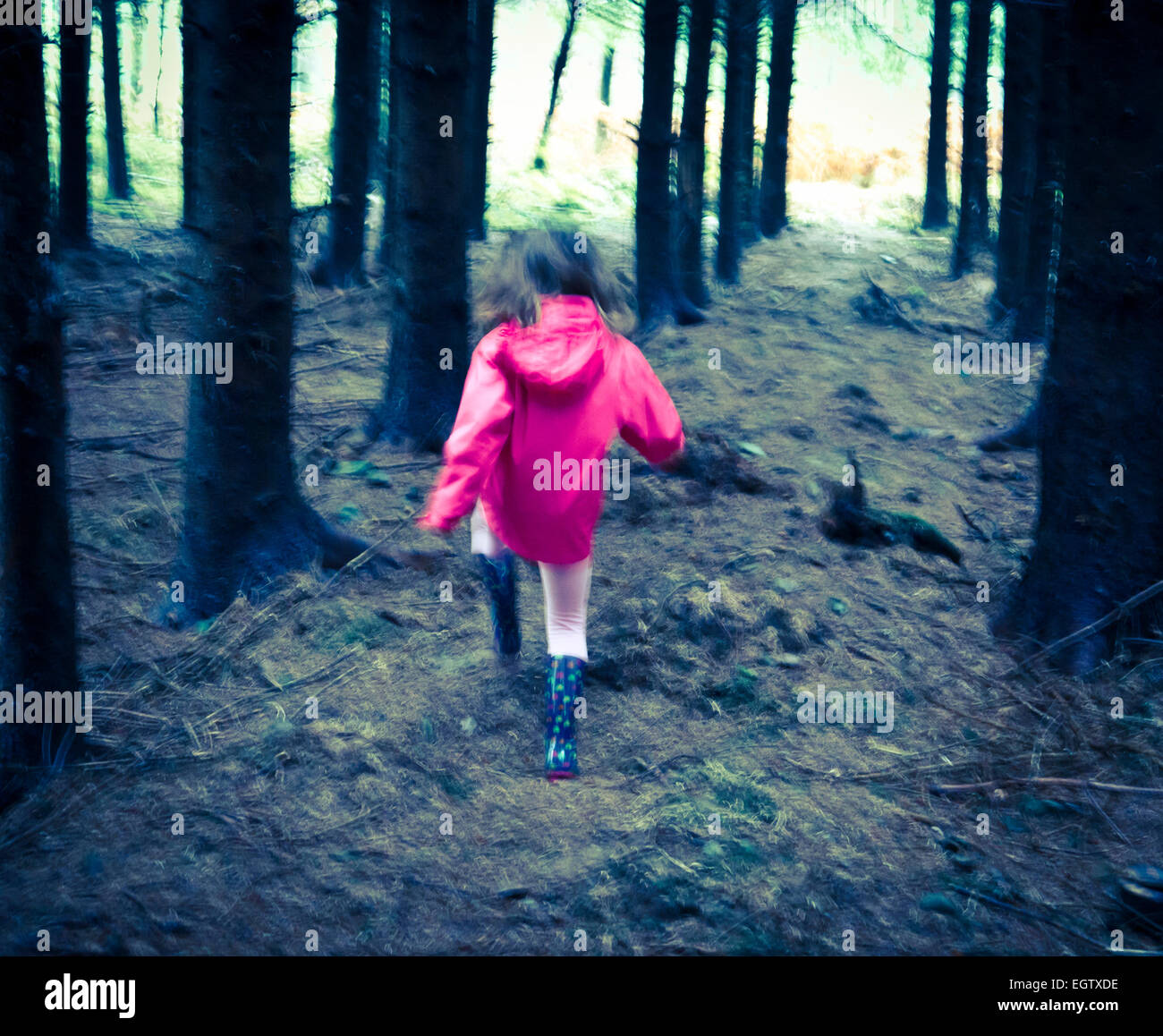 Young girl in pink coat running towards light out of forest. Stock Photo