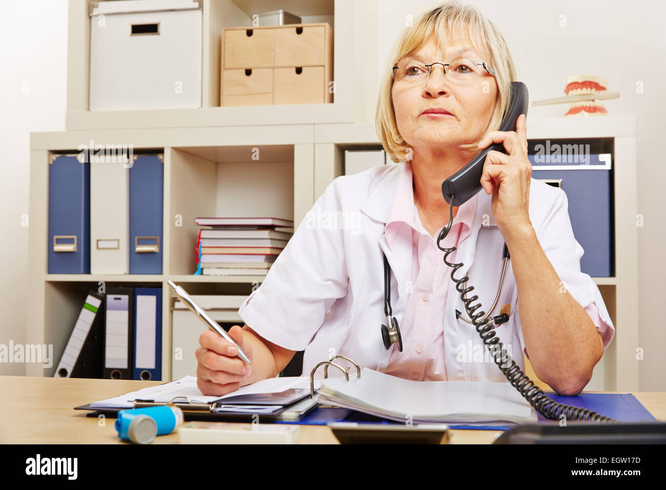 Elderly female doctor sitting at emergency service telephone in the office Stock Photo