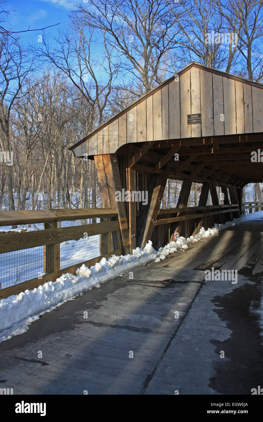 Road leading to covered bridge on sunny snow covered day at the park Stock Photo