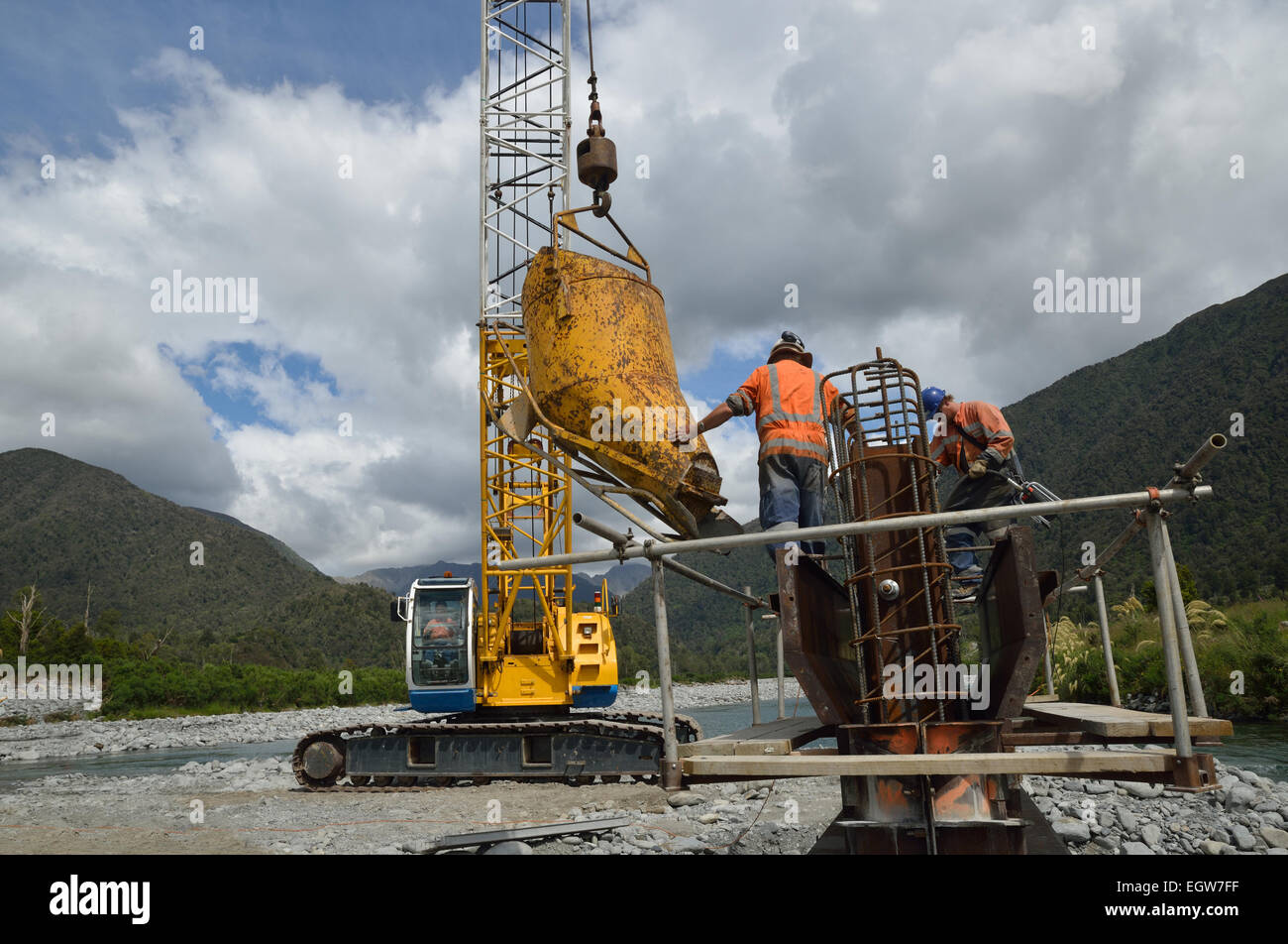 Builders pour concete into the pylon of a concrete bridge over a small river in Westland, New Zealand Stock Photo