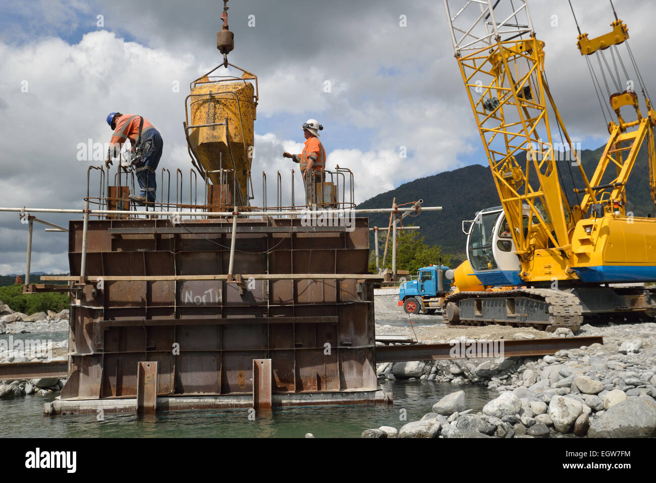 Builders pour concrete into the foundations of a concrete bridge over a small river in Westland, New Zealand Stock Photo